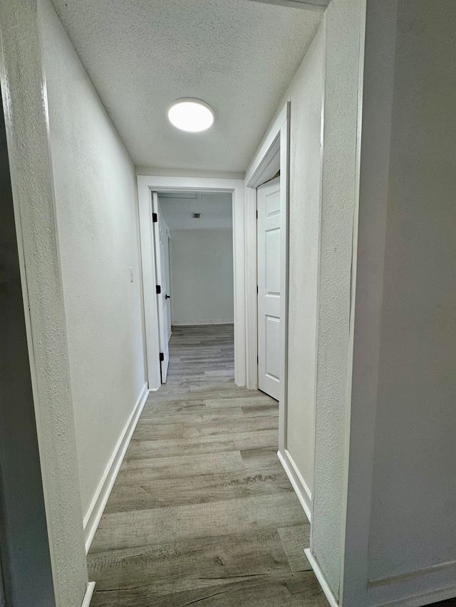 hallway featuring baseboards, a textured wall, a textured ceiling, and wood finished floors