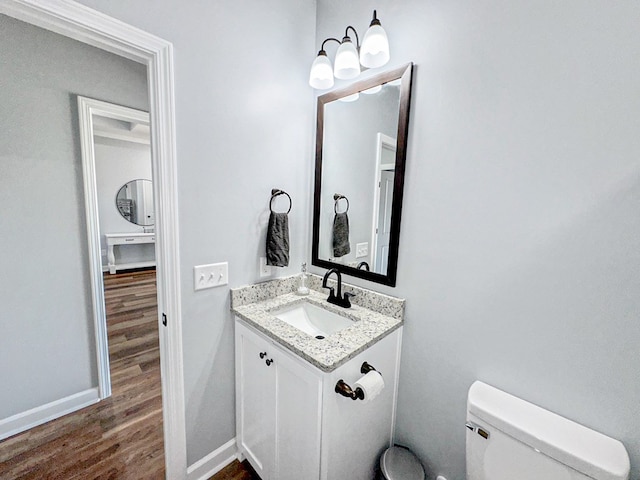 half bathroom with vanity, baseboards, toilet, and wood finished floors