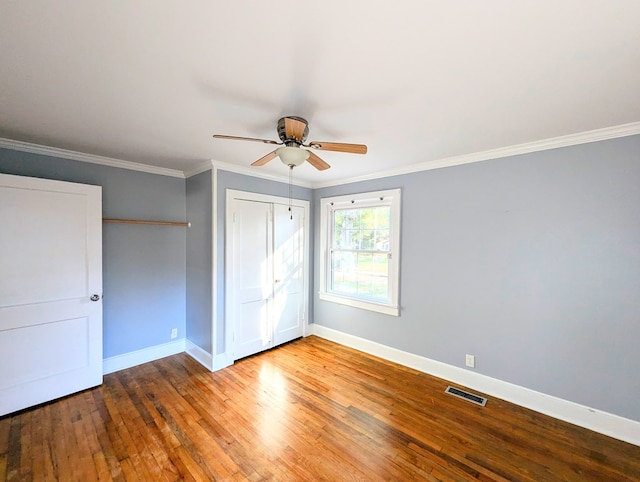 unfurnished bedroom with ceiling fan, wood-type flooring, ornamental molding, and a closet