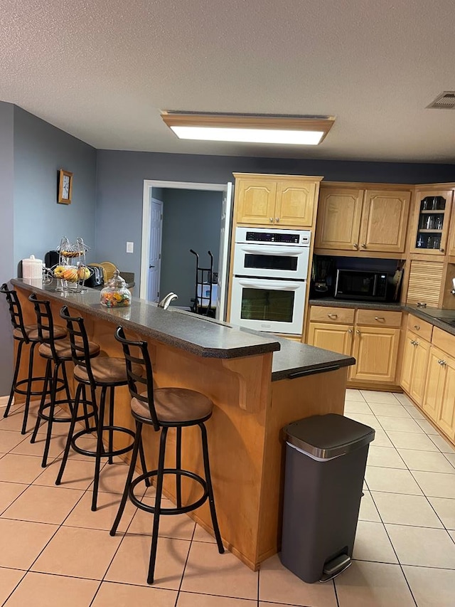 kitchen with a textured ceiling, white double oven, light tile patterned floors, and a breakfast bar area