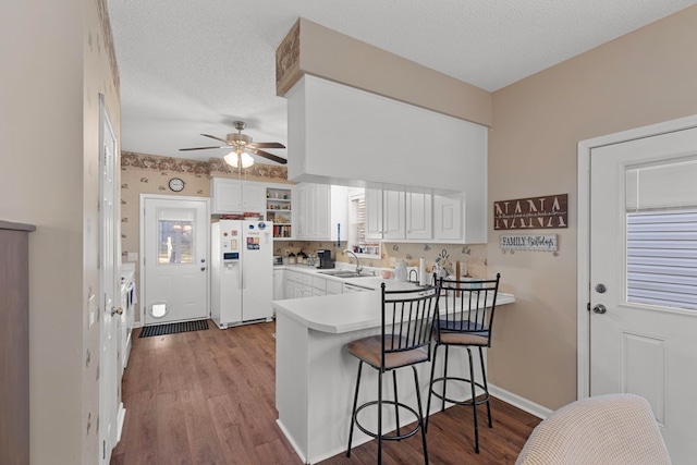 kitchen with kitchen peninsula, hardwood / wood-style floors, white cabinets, and white refrigerator with ice dispenser