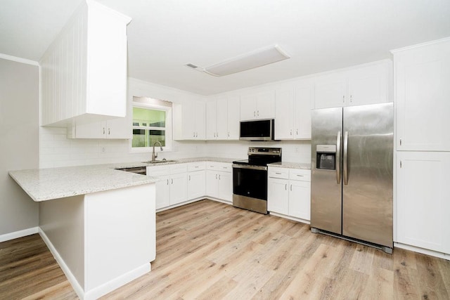 kitchen with a sink, appliances with stainless steel finishes, a peninsula, light wood finished floors, and white cabinetry