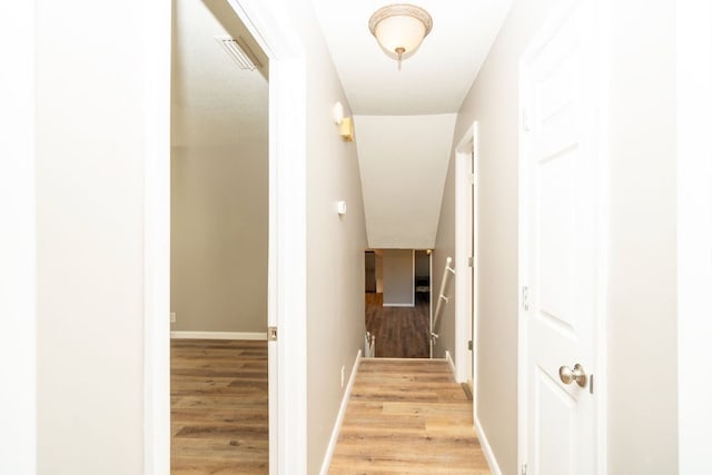 hall with visible vents, baseboards, and light wood finished floors