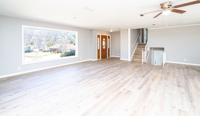 unfurnished living room featuring stairway, light wood-style flooring, baseboards, and ceiling fan
