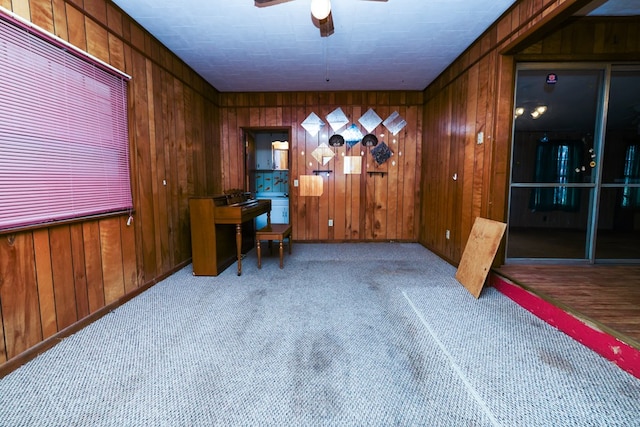 carpeted home office featuring wooden walls and ceiling fan