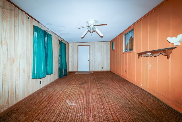 carpeted spare room featuring ceiling fan and wood walls