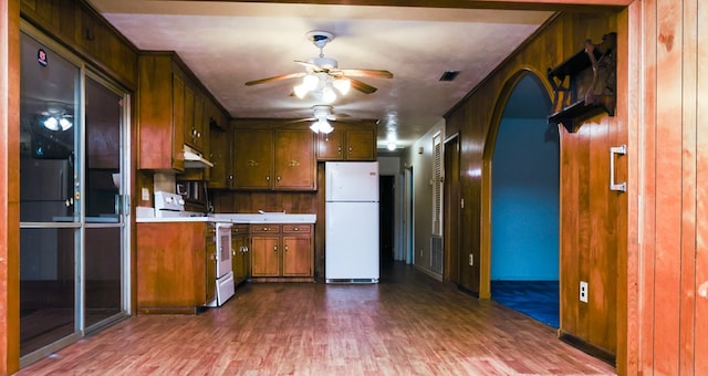 kitchen with dark wood-type flooring, under cabinet range hood, white appliances, arched walkways, and light countertops