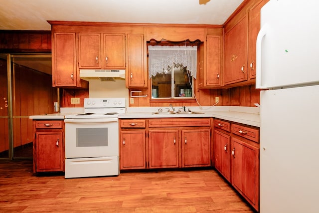 kitchen with brown cabinets, light wood-style flooring, under cabinet range hood, a sink, and white appliances