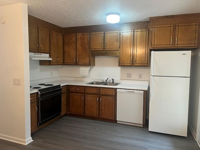 kitchen featuring white appliances, brown cabinetry, light countertops, under cabinet range hood, and a sink