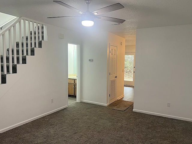 empty room with dark carpet, stairway, ceiling fan, a textured ceiling, and baseboards