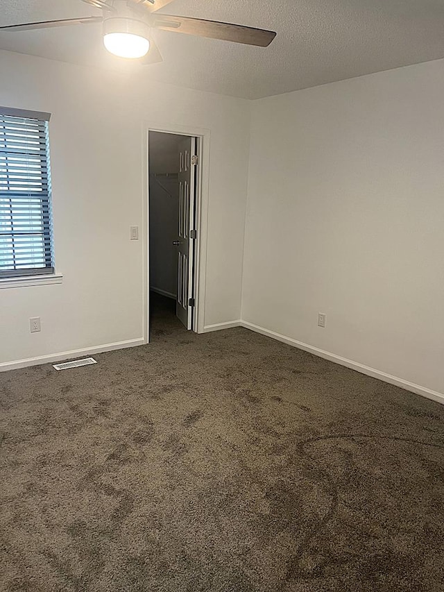 unfurnished room featuring baseboards, visible vents, ceiling fan, a textured ceiling, and dark carpet