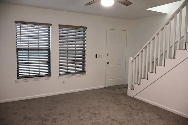 foyer featuring stairway, dark carpet, a ceiling fan, and baseboards