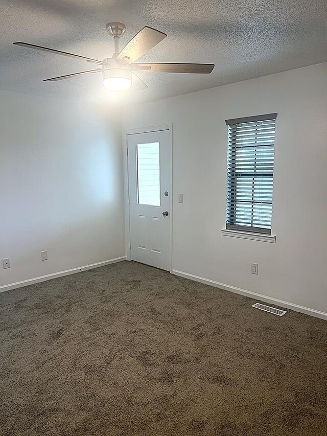 unfurnished room featuring baseboards, visible vents, dark carpet, and a ceiling fan