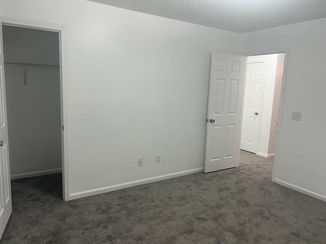 unfurnished bedroom featuring a textured ceiling, dark colored carpet, a closet, and a walk in closet