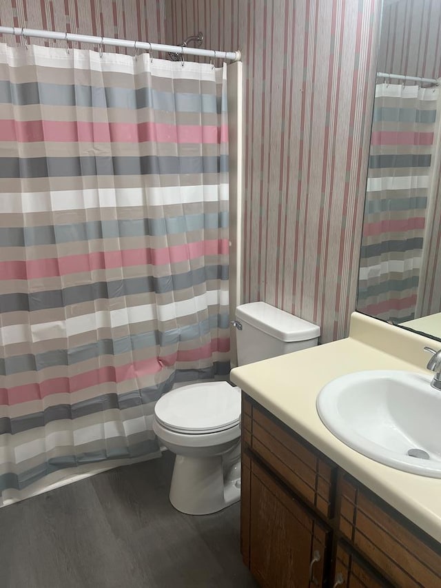 full bath featuring toilet, wallpapered walls, wood finished floors, and vanity