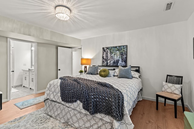 bedroom with ensuite bathroom, a chandelier, and light hardwood / wood-style floors