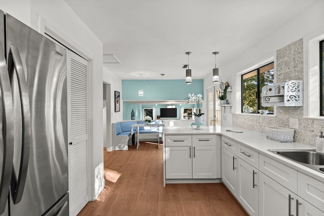 kitchen with white cabinetry, stainless steel fridge, kitchen peninsula, dark hardwood / wood-style floors, and pendant lighting