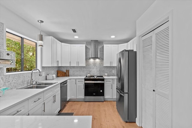 kitchen with pendant lighting, sink, white cabinetry, stainless steel appliances, and wall chimney exhaust hood