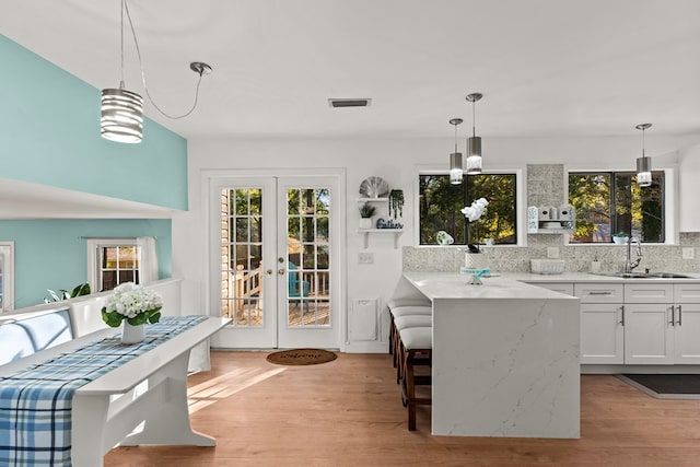 kitchen with pendant lighting, white cabinetry, french doors, tasteful backsplash, and sink