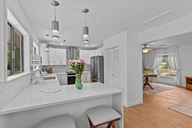 kitchen featuring wall chimney exhaust hood, white cabinetry, stainless steel appliances, sink, and kitchen peninsula