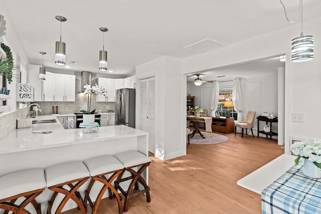 kitchen featuring wall chimney range hood, kitchen peninsula, sink, stainless steel refrigerator, and white cabinetry