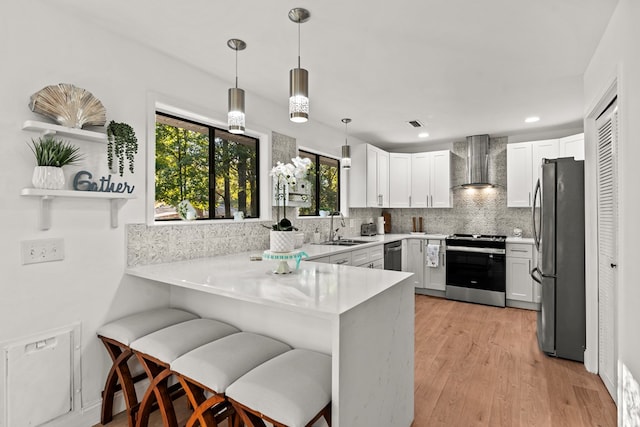 kitchen featuring sink, kitchen peninsula, wall chimney range hood, and stainless steel appliances