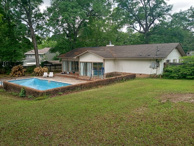 rear view of property with a sunroom, a patio area, a lawn, an outdoor pool, and fence