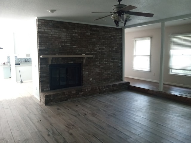 unfurnished living room with baseboards, wood finished floors, a ceiling fan, and a fireplace