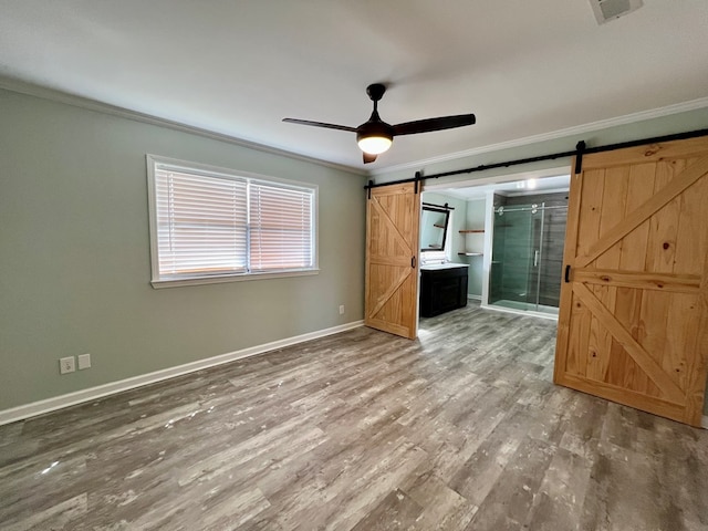 unfurnished bedroom featuring a barn door, baseboards, connected bathroom, wood finished floors, and crown molding