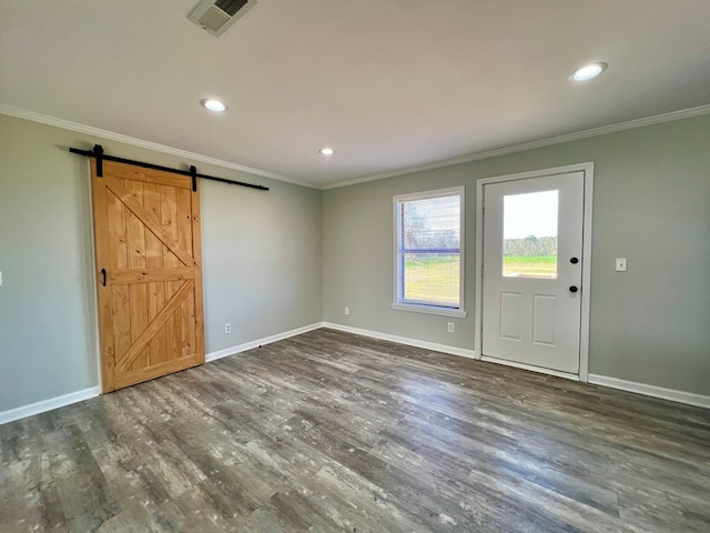 entrance foyer with a barn door, visible vents, wood finished floors, and ornamental molding
