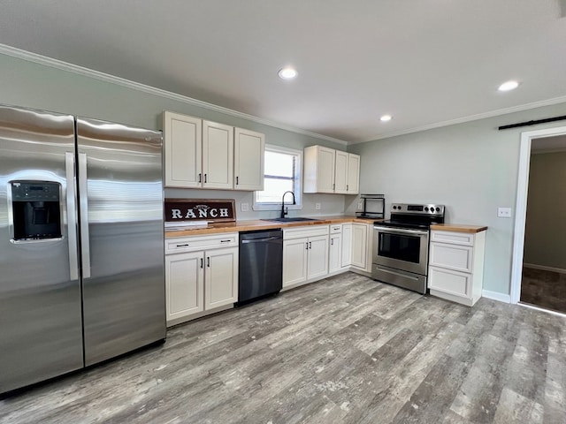 kitchen with stainless steel appliances, butcher block counters, a sink, light wood-style floors, and crown molding