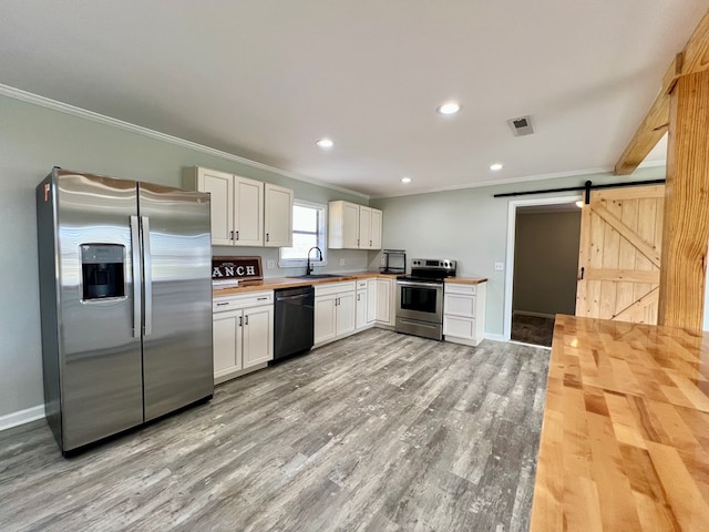 kitchen with a barn door, white cabinets, appliances with stainless steel finishes, ornamental molding, and light wood-style floors