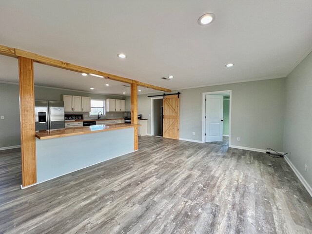 kitchen featuring stainless steel refrigerator with ice dispenser, a barn door, a sink, wood finished floors, and a peninsula