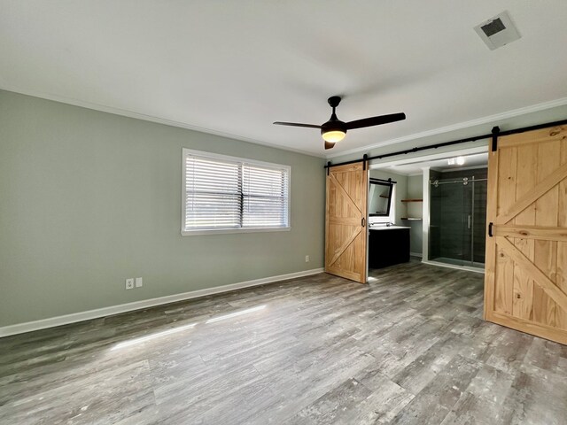 unfurnished bedroom with a barn door, wood finished floors, visible vents, baseboards, and crown molding