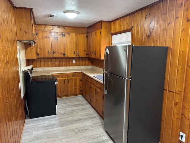 kitchen with stainless steel fridge, stove, light hardwood / wood-style floors, and a textured ceiling