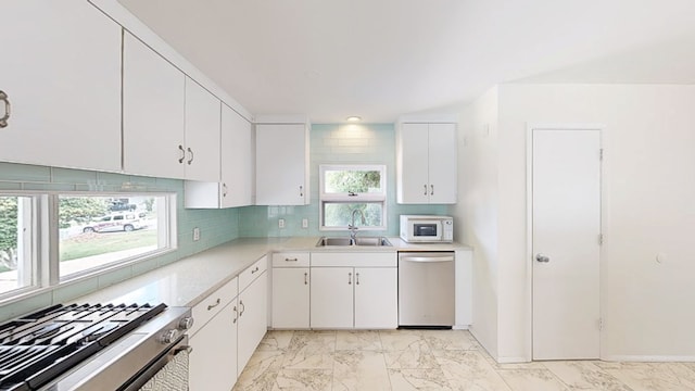 kitchen featuring a sink, appliances with stainless steel finishes, light marble finish floors, and light countertops
