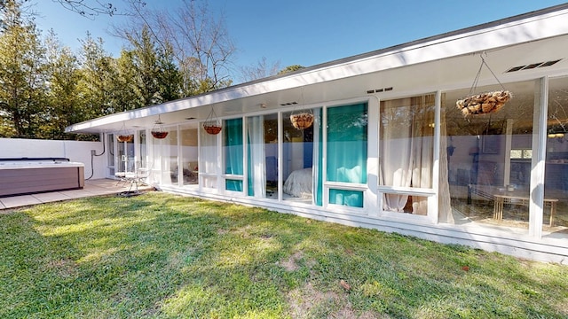 rear view of house with a hot tub and a lawn