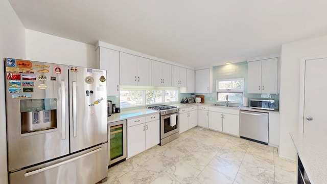 kitchen with beverage cooler, stainless steel appliances, white cabinetry, light countertops, and marble finish floor