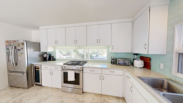 kitchen featuring marble finish floor, backsplash, appliances with stainless steel finishes, a sink, and beverage cooler