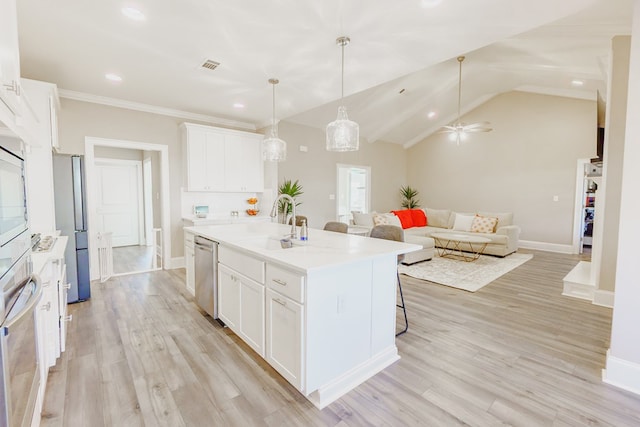 kitchen featuring stainless steel appliances, white cabinets, an island with sink, and decorative light fixtures