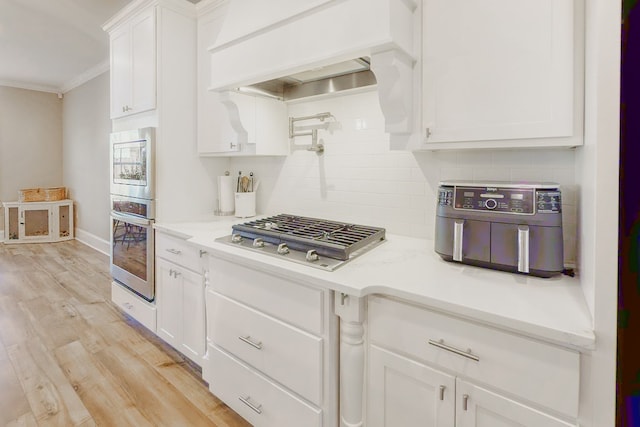 kitchen featuring white cabinetry, tasteful backsplash, stainless steel gas stovetop, custom exhaust hood, and ornamental molding