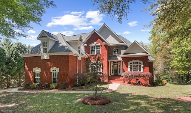 view of front facade with a shingled roof, a front lawn, and brick siding
