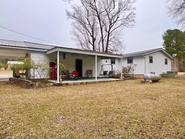 rear view of property with metal roof, a patio, central AC unit, and a lawn