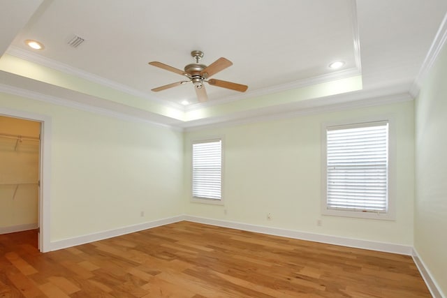 empty room featuring visible vents, baseboards, light wood-style floors, ornamental molding, and a tray ceiling