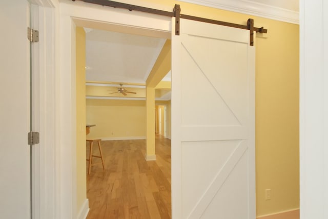 corridor featuring light wood finished floors, a barn door, baseboards, and crown molding