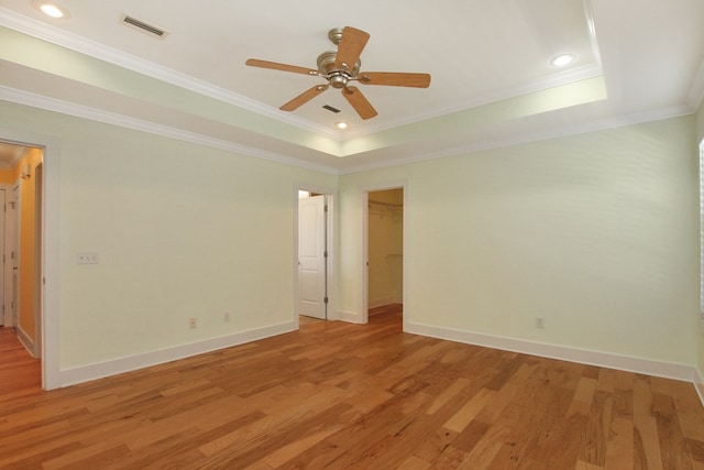 empty room featuring a raised ceiling, visible vents, ornamental molding, light wood-type flooring, and baseboards