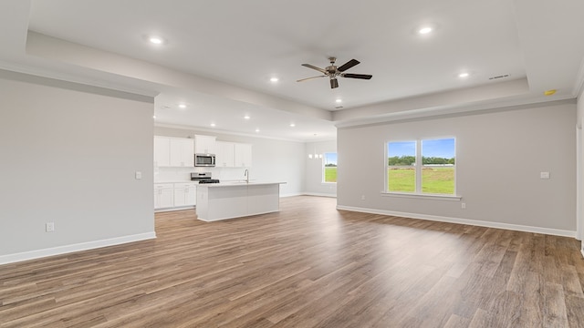 308 Heritage Way, Headland, AL 36345 - unfurnished living room with a ceiling fan, a raised ceiling, light wood-style flooring, and baseboards