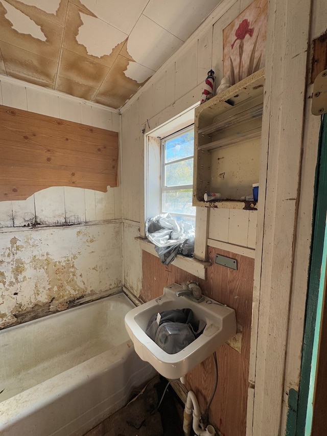 bathroom featuring sink, a bath, and wooden walls