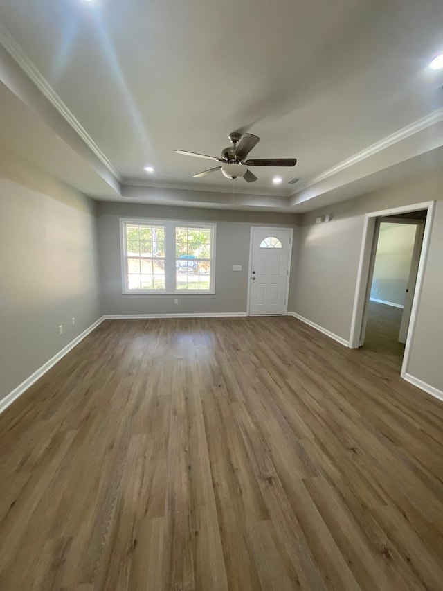 unfurnished living room with hardwood / wood-style floors, a raised ceiling, ceiling fan, and ornamental molding