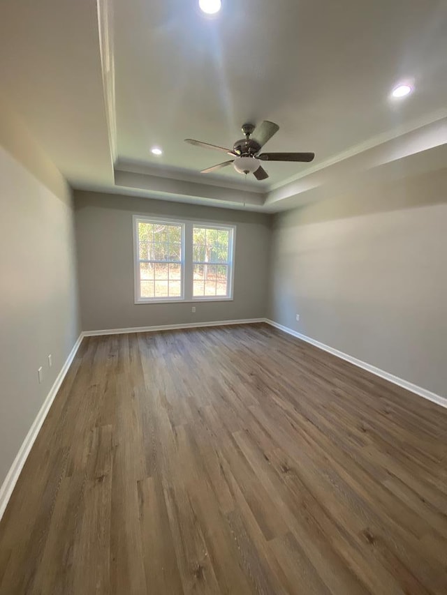 empty room featuring a raised ceiling, ceiling fan, and dark hardwood / wood-style flooring